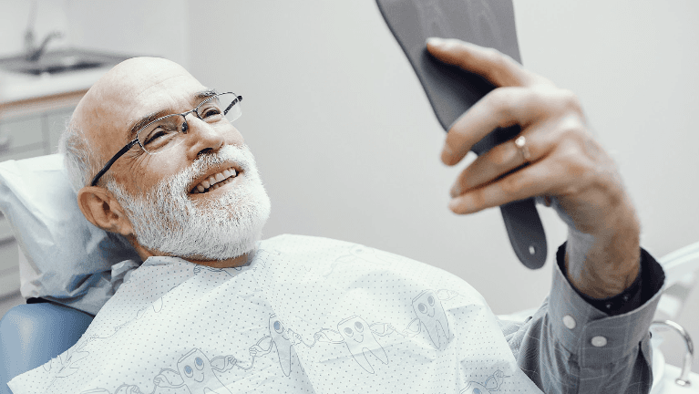 Man sitting in a dental chair while holding a mirror