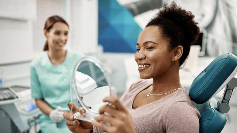 woman sitting in a dental chair while holding a mirror